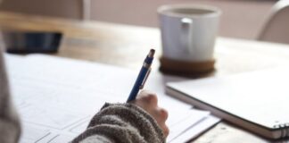 person writing on brown wooden table near white ceramic mug