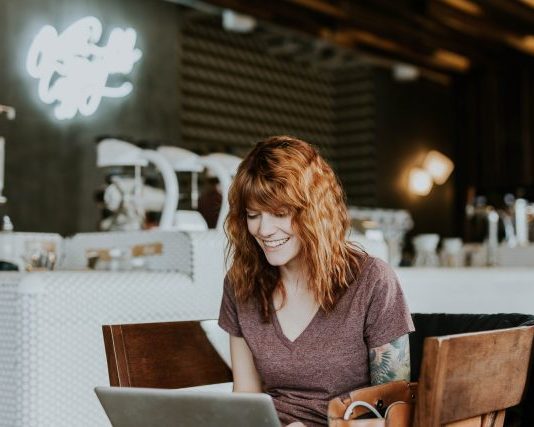 woman sitting on brown wooden chair while using silver laptop computer in room