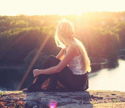 woman sitting on brown surface watching at body of water