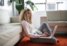 woman sitting on floor and leaning on couch using laptop