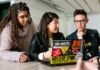 three people around a laptop with stickers on it