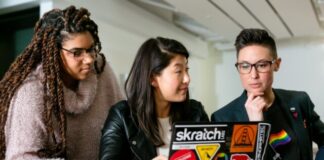 three people around a laptop with stickers on it