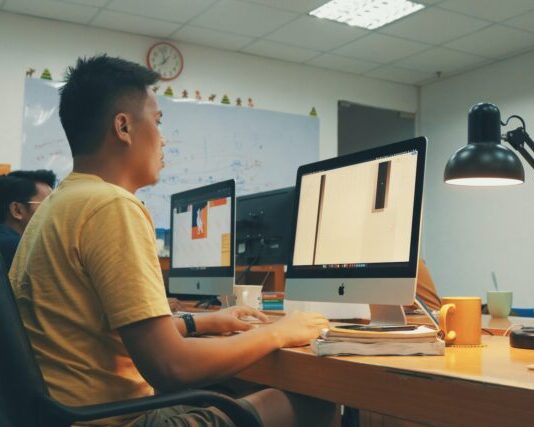 man using Apple desktop inside room beside man