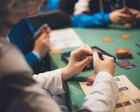 Crop people playing cards at table