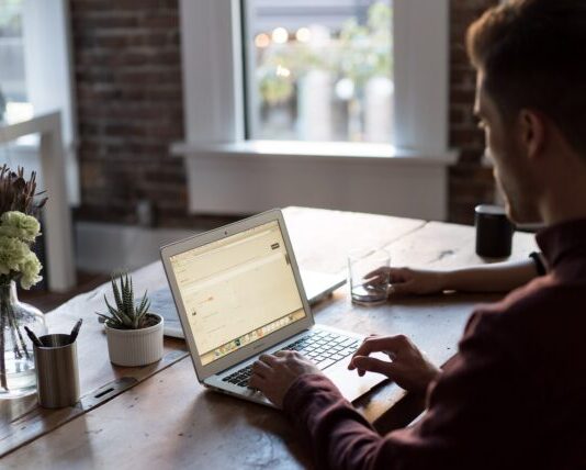 टेबलको शीर्षमा ल्यापटप सञ्चालन गर्ने मानिस