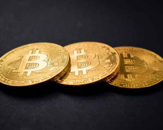 three gold-colored bitcoins on black surface