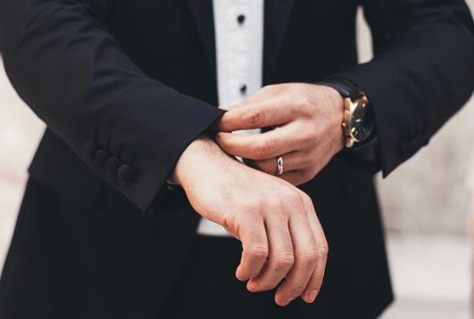 A man's hands adjusting the cuffs of his black suit