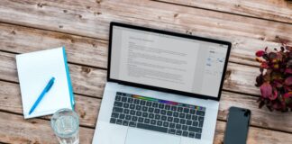 silver MacBook beside space gray iPhone 6 and clear drinking glass on brown wooden top