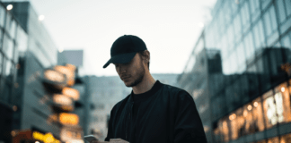 A man in a black jacket wearing a black fitted cap while using a phone