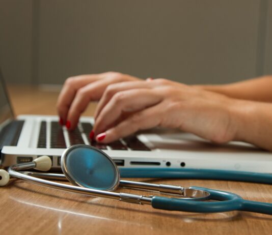 person sitting while using laptop computer and green stethoscope near