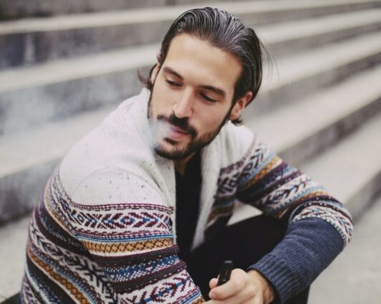 man in white sweater holding black smartphone