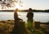 man in black jacket standing beside body of water during sunset