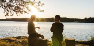 man in black jacket standing beside body of water during sunset