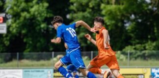 man in blue and orange jersey shirt running on green grass field during daytime