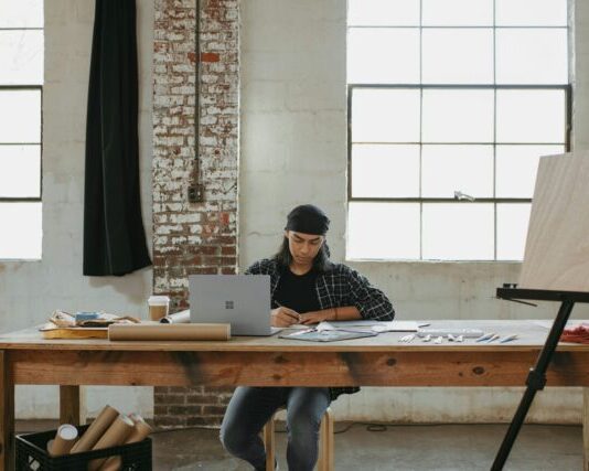 مردی پشت میز نشسته و روی لپ تاپ کار می کند