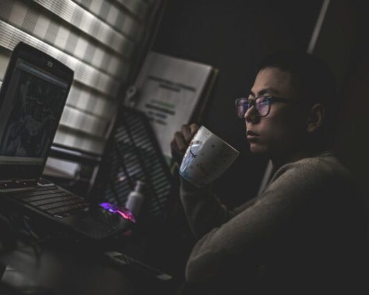 man holding mug in front laptop computer