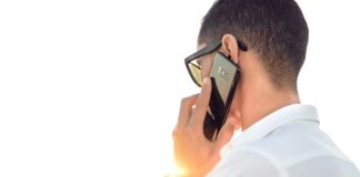 man holding smartphone standing in front of calm body of water