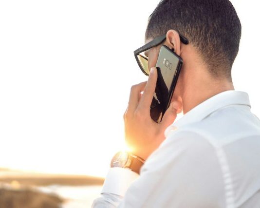 man holding smartphone standing in front of calm body of water