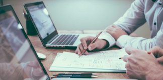 person holding pencil near laptop computer