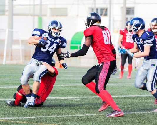 football players in red jersey shirt and red pants running on green grass field during daytime