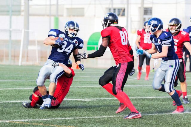 Photo by Quino Al football players in red jersey shirt and red pants running on green grass field during daytime